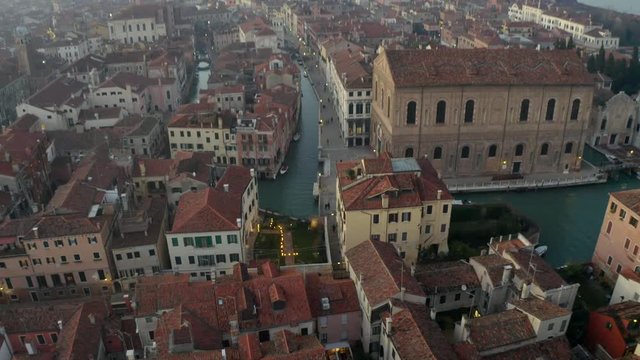 Aerial, descending, drone shot towards buildings and a small channel, on a sunny evening, in Venezia, Italy