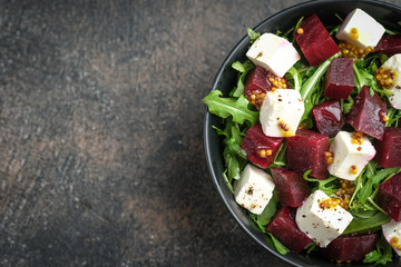 Salad with beetroot, feta cheese, arugula and spicy dressing on a dark background. Healthy food. Top view. Copy space.