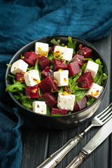 Salad with beetroot, feta cheese, arugula and spicy dressing on a dark background. Healthy food.
