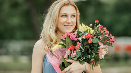beautiful woman with a bouquet of flowers standing on the grass in the city Park