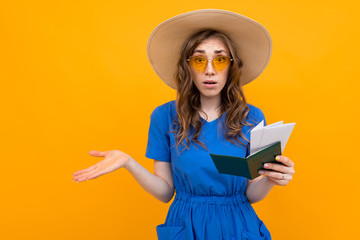 happy surprised girl in a blue dress and a straw hat and sunglasses with a passport and vacation tickets on a yellow background