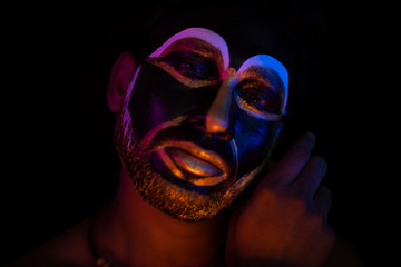 Close up of Indian brunette man with his face illuminated and painted by black and golden like a tribe standing with candle light in front of a black studio copy space background. Indian hi fashion.
