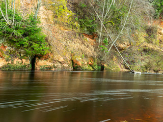 a landscape with a steep river and caves on a sandstone cliff