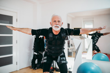 Nice looking and positive senior man doing exercises in electrical muscular stimulation suit.