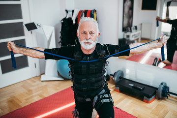 Nice looking and positive senior man doing exercises in electrical muscular stimulation suit. - obrazy, fototapety, plakaty