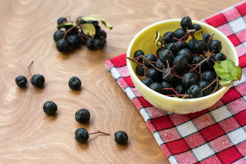 Ripe black chokeberries (aronia melanocarpa) in a white bowl on red napkin on wooden table. Bowl full of freshly picked homegrown aronia berries.