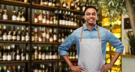 people, job and profession concept - smiling indian barman or waiter in apron over wine bar...