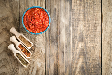 Traditional spicy harissa sauce in oriental bowl on rustic light background with spices. Maghreb cuisine. Top view with copy space.