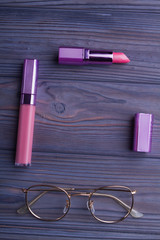Fototapeta premium Red lipstic, mascara and glasses on wood. Flat lay, top view, copyspace, free space for text.