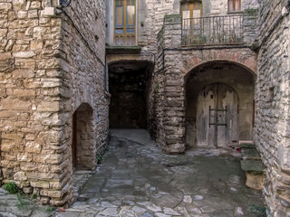 Fototapeta na wymiar Spain, Montfalco Murallat - October 10, 2018: Old wooden gate in the stone walls of buildings in Montfalco Murallat village in Lleida province. Medieval houses with doors in a Spanish tourist place