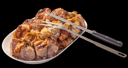 Spit Roasted Pork Meat Slices Offered on Oblong Porcelain Tray with Serving Knife and Fork Isolated on Black Background
