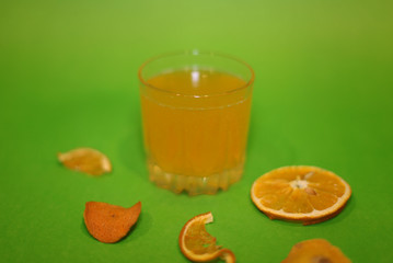 Glass with orange soda and decor of orange and orange crusts, on a green background.