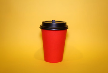 Paper Cup with a black lid for coffee and cappuccino stands on a bright yellow background, minimalism.
