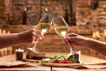 Female's hands toasting with glasses of white wine over table. Women's friendship