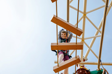 Happy little kid boy climbing on high rope course trail. Active child making adventure and action on family vacations. Challenge for brave kids.
