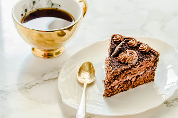 Chocolate cake on a white plate and yellow gold cup of tea. Selective focus