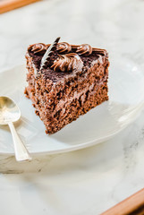 Chocolate cake on a white plate and yellow gold cup of tea. Selective focus