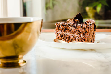 Dark Chocolate cake on a white plate and yellow gold cup of tea. Selective focus. Sweet dessert.