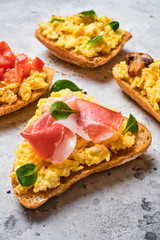 Scramble omelet sandwiches, bacon, mushrooms, tomatoes and fresh herbs on a light gray background.