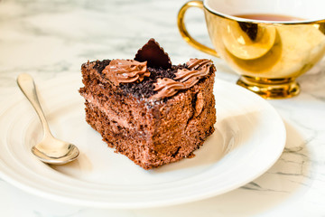 Piece of chocolate cake in a white plate and gold cup of coffee, closeup. Selective focus. Seasonal and holidays pattern