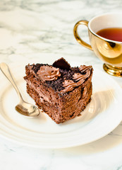 Piece of chocolate cake in a white plate and gold cup of coffee, closeup. Selective focus. Seasonal and holidays pattern