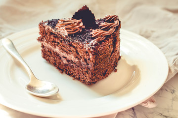 Piece of chocolate cake in a white plate and gold cup of coffee, closeup. Selective focus. Toning.