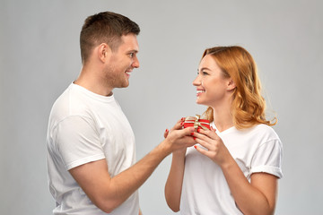 relationships, holiday and valentines day concept - happy couple in white t-shirts with christmas gift over grey background