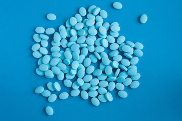 Blue pills or vitamins are scattered on a blue background. Medicine and health.