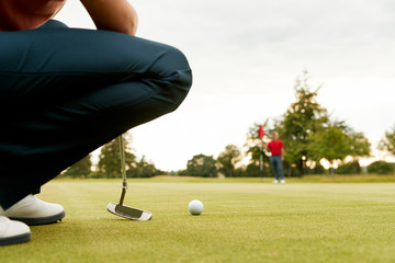 Close Up Of Female Golfer Lining Up Shot On Putting Green As Man Tends Flag