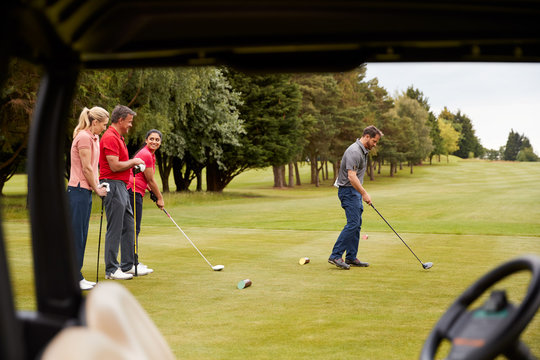 Two Couples Golfing Hitting Tee Shot Along Fairway With Driver With Buggy In Foreground