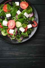 Fresh vegetable salad with feta, olives and herbs in a dark plate on a dark rustic background. Healthy vegan food. Top view copy space.