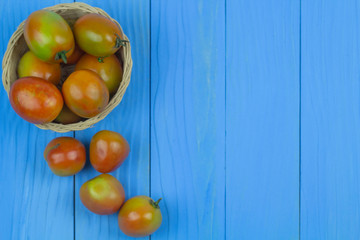 Fresh tomatoes in the basket on the blue wooden table