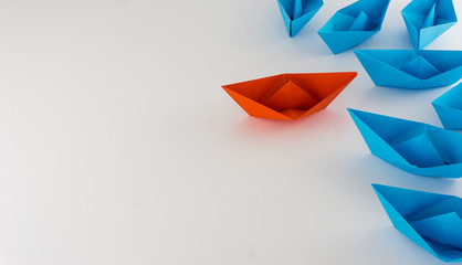Red boat origami leading a group of blue boats origami leadership concept
