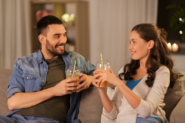 drinks and people concept - happy couple drinking takeaway juice from plastic cups with paper straws at home in evening