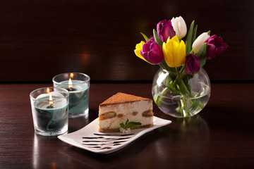 tasty fresh tiramisu cake on a brown background with a bouquet of tulips