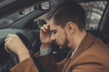 a young man of thirty years, holding his head, having a headache, driving a car. Poor health while...