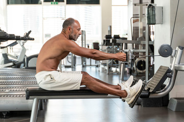 Muscular shirtless mature older bodybuilding athlete with balding gray hair rowing exercise on a...