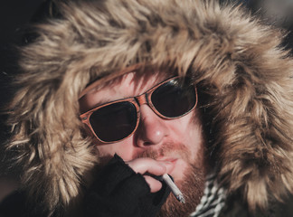 Handsome hipster stylish man smoking outside in urban setting,