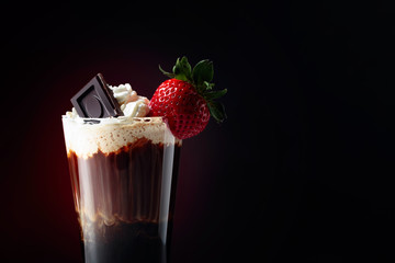 Coffee cocktail with whipped cream, strawberry and pieces of black chocolate on a dark background.