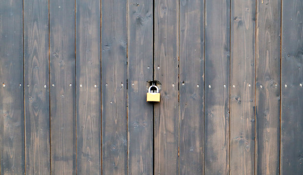 Wooden surface of old textured brown planks closed on a rusted lock close up. Old wooden gate with a metal lock. brown wooden door with a lock