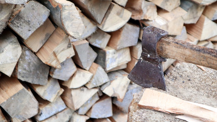Chipped firewood for the winter for heating. The ax is stabbed with a blade into the stump. Cleaver with a wooden handle. Harvesting on the farm. Dry firewood stacked in piles for heating a house