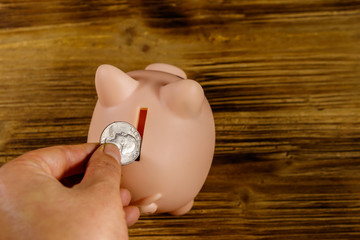 Hand putting coin into pink piggy bank. Saving money concept