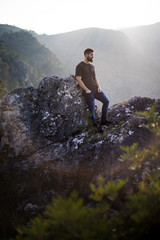 Man on a rock at the mountains with the sun behind