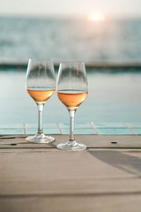 Two glasses of wine  on the edge of infinity swimming pool with panoramic views of the sea at sunset. Drink, celebrate, vacation and summer concept.