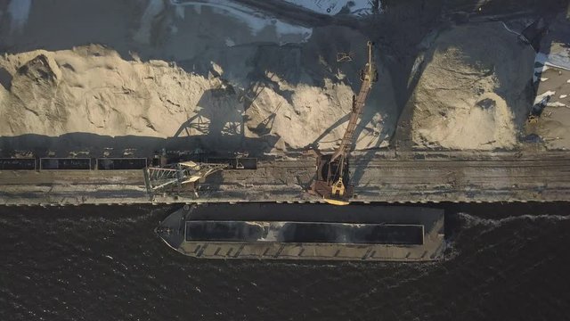 Large port cranes on the shore near the pier unload the river sand barge onto a large heap. The train for the transport of bulk cargo. The work of the cargo port. Aerial photography drone quadrocopter