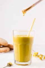 golden milk in which honey is poured from a wooden spoon