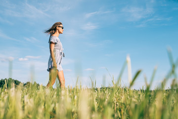 Young woman walking in the green sunny field