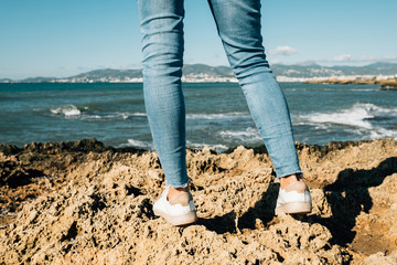 Woman's legs in jeans back view on the sea coast