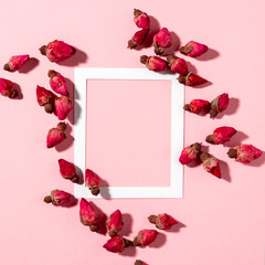 Flatlay of dried rose flowers on a pink background and white paper frame with copy space, hard flashlight