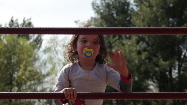 Little girl with pacifier climbs up metal bars at park, Slowmo Closeup